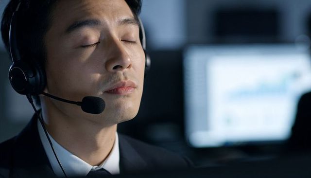 Calm asian customer support agent resting with headset at night office workstation