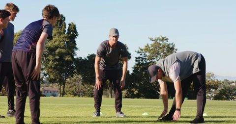 Coach guiding diverse athletes stretching for agility and team fitness on training field