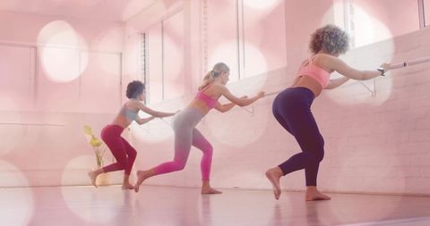Practicing barre workout in sunlit pastel studio, trio of women barefoot exercising