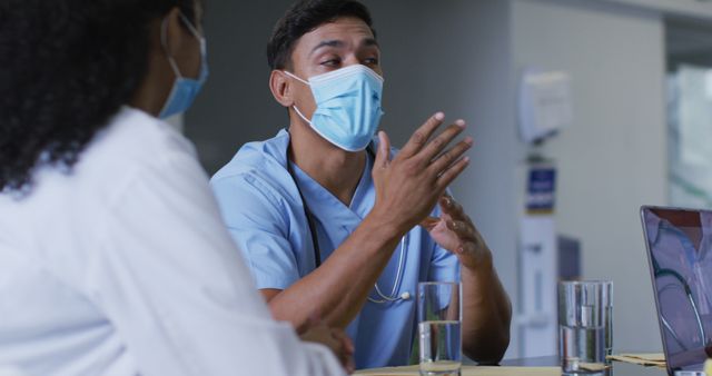 Biracial male doctor and female hospital colleague wearing face masks talking at meeting. medicine, health and healthcare services during covid 19 coronavirus pandemic.