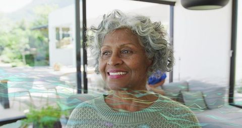 Smiling senior woman standing by glass doors with digital waveforms conveying wellness and resilienc