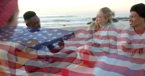 Friends enjoying beach sunset playing acoustic guitar and holding red cups with american flag overla