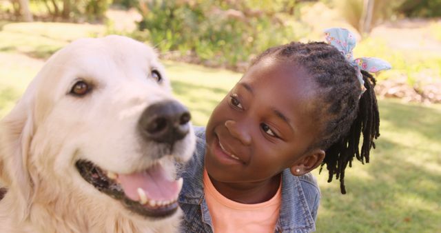 Shows a smiling African American girl enjoying an afternoon with her Golden Retriever in a park. Ideal for concepts of childhood, pet companionship, nature outings, and pet-friendly family activities.