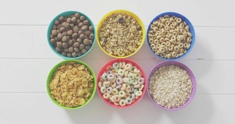 Colorful Bowls Displaying Assorted Breakfast Cereals in Neat Grid on White Wooden Tabletop