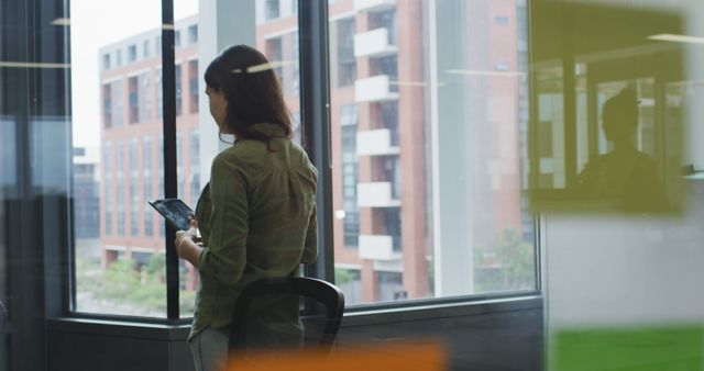 Businesswoman Holding Tablet Looking Through Office Window in Modern Building - Download Free Stock Images Pikwizard.com