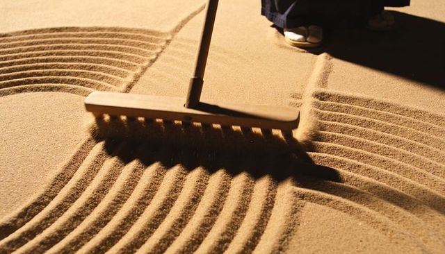 Zen garden raking creating sand patterns with wooden rake, meditative ritual texture