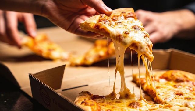 Lifting stretching cheese pizza slice from open cardboard box with stringy melted cheese