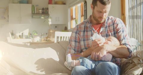 Loving father feeding baby in sunlit home