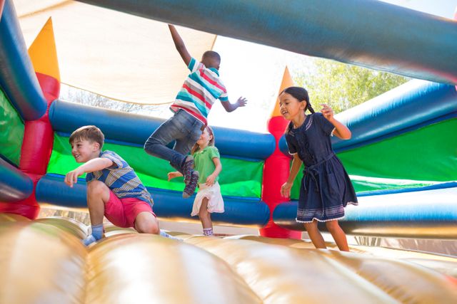 Children are having fun jumping on a colorful bouncy castle at a playground. This image is perfect for illustrating outdoor activities, childhood joy, and group play. It can be used in advertisements for playgrounds, summer camps, or children's events, as well as in educational materials about physical activity and social interaction.