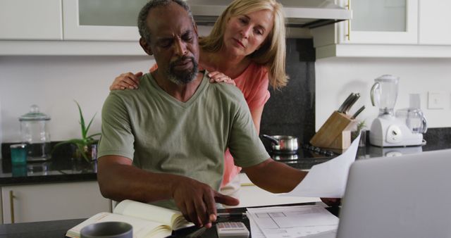Couple reviewing home finances in kitchen, reflecting a scene of financial planning and budgeting. Ideal for themes related to personal finance, family budgeting, retirement planning, or discussing work-life balance. Useful for blog posts, articles, financial service advertisements, and promotional materials targeting mature audiences.
