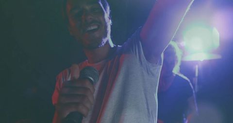 Lead singer raising arm while holding microphone under blue stage lights
