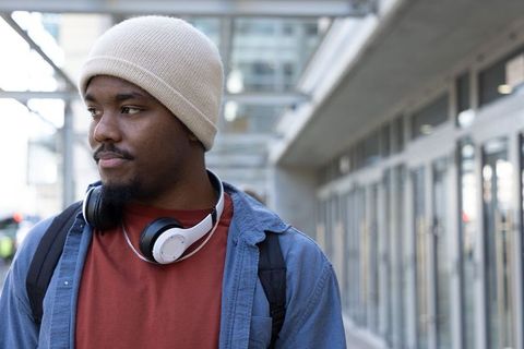 Thoughtful african american commuter wearing beanie and headphones on urban walkway