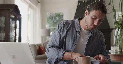 Man writing notes at home office with laptop and coffee mug