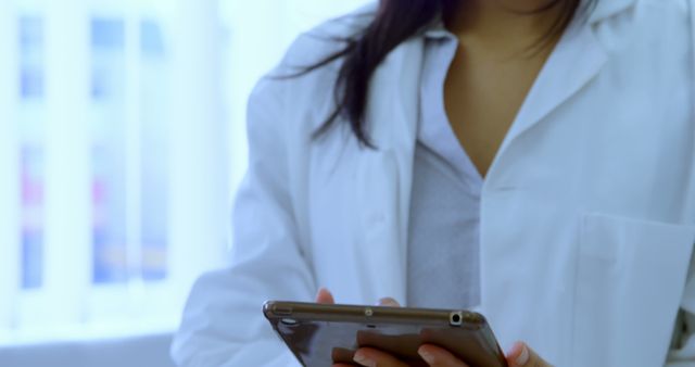 This image depicts a female medical professional using a tablet, foreground light background. Lab coat signifies healthcare setting, ideal for illustrating modern healthcare concepts, professional practice, digital healthcare solutions, hospital environment, use in medical or educational materials.