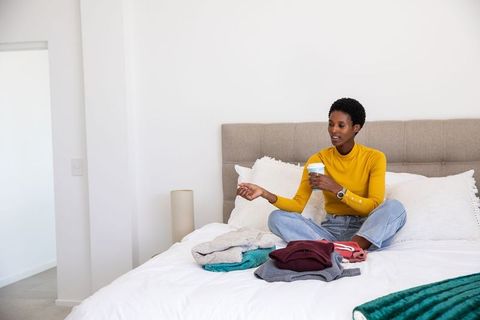 Woman relaxing on bed with coffee sorting clothes