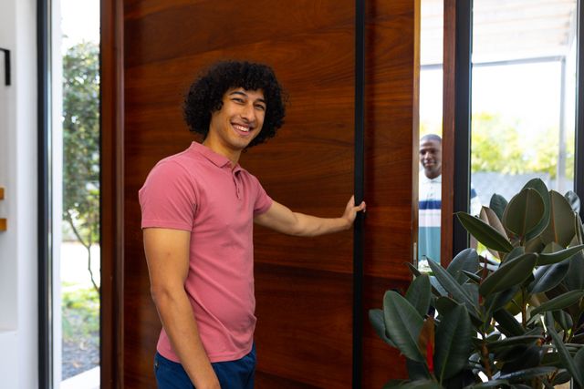 Portrait of smiling biracial man opening front door for visiting friends, copy space. Domestic life, friendship and togetherness concept.