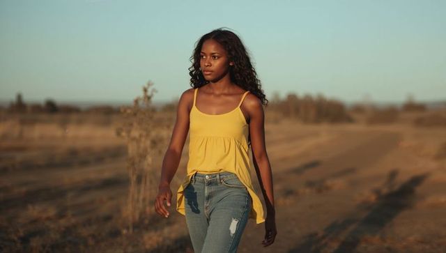 Young woman walking along rural dirt trail at golden hour wearing yellow tank top