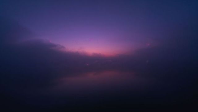 Minimalist twilight seascape glowing on horizon with indigo purple mist and mirrored water