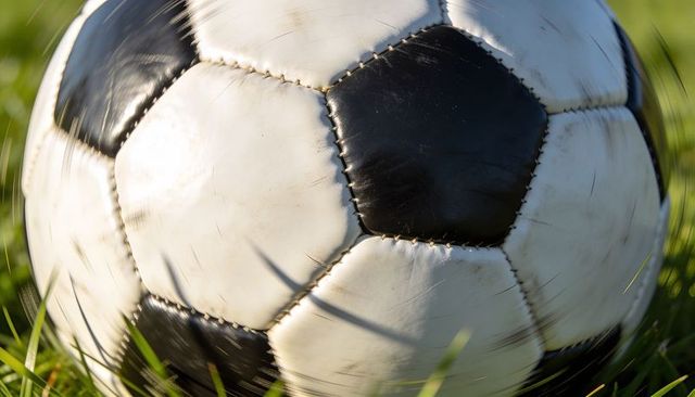 Sunlit worn black-and-white soccer ball resting on grass with visible stitches and scuffs