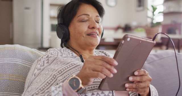 African american senior woman wearing headphones listening to music on digital tablet at home. retirement lifestyle living concept