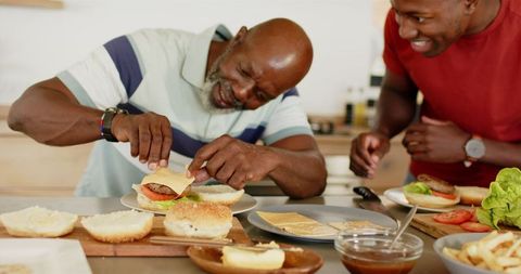 Mature Man and Friend Happily Preparing Burgers in Kitchen