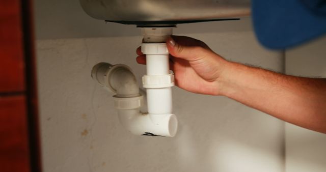 Plumber repairing kitchen sink drain pipe, ideal image for articles, blogs, and manuals about home maintenance, plumbing tips, or DIY repair guides. Can be used by plumbing services and technician advertisements.