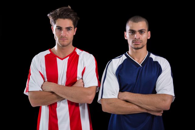 Two football players in uniforms standing with arms crossed against a black background. Ideal for use in sports promotions, team posters, competition announcements, and athletic event marketing materials.