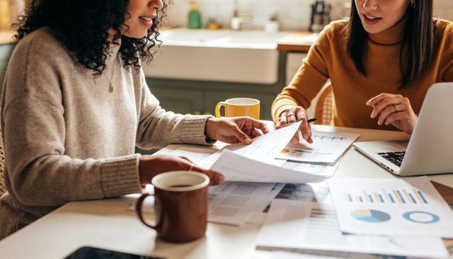 Remote colleagues reviewing charts and financial reports at kitchen table with laptop