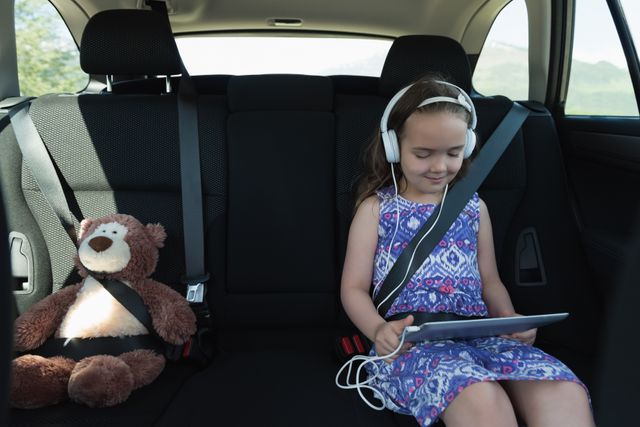 Cute girl listening music on headphone from digital tablet in car