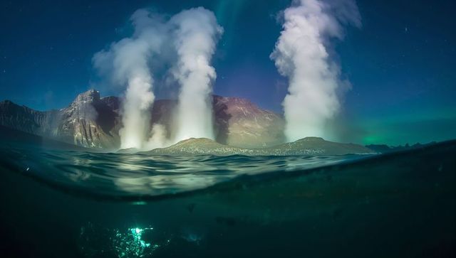 Three towering steam columns rising from volcanic islet at night under aurora borealis