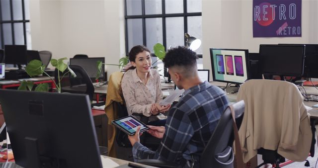 Colleagues in a modern office engaged in a creative discussion about design, with computers and tablets visible. This image can be used for concepts related to teamwork, collaboration, creative professions, office life, and modern work environments.