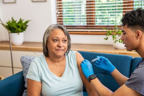 Senior woman receiving vaccine from healthcare worker at home