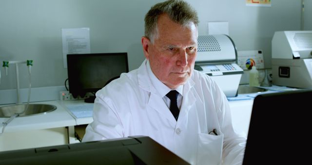 Senior scientist in laboratory wearing a white lab coat, using computer. Suitable for illustrating scientific research, laboratory work, professional scientists at work, technological advancements in science, STEM education materials.
