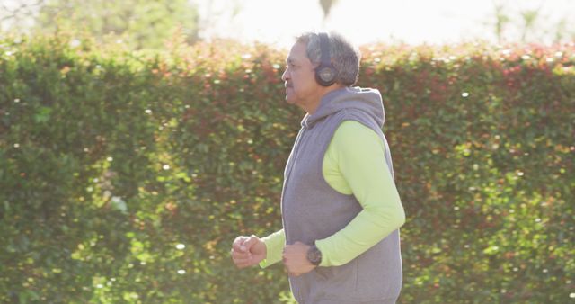 Image of senior biracial man in sports clothes and headphones running in street. Retirement, hobbies, health, inclusivity and active senior lifestyle concept.
