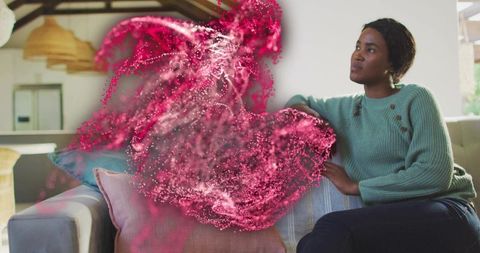 Woman on sofa gazing at futuristic pink particle swirl in sunlit living room