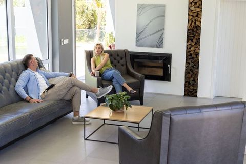 Couple chatting and relaxing in modern sunlit living room with fireplace and large windows