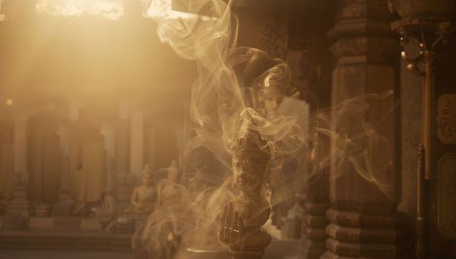 Ornate deity bust emitting curling incense smoke, warm backlit shrine interior