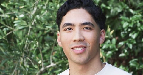 Young asian man smiling in garden headshot looking at camera natural light closeup