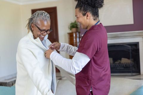 Home caregiver fastening jacket for african american senior woman showing compassionate care