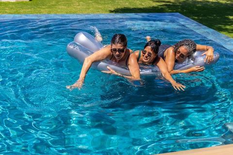 Women lounging on silver inflatable in backyard pool splashing turquoise water