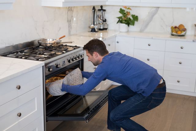 Man placing pizza into oven in modern kitchen. Ideal for content related to home cooking, culinary skills, kitchen appliances, and domestic lifestyle. Suitable for blogs, cooking websites, and advertisements for kitchen products.