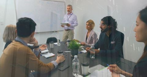 Executive presenting strategy to diverse team in modern boardroom with laptops and coffee