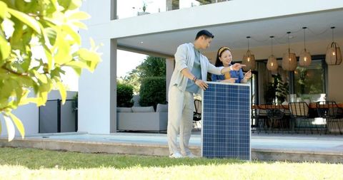 Asian couple installing solar panel on modern patio for residential renewable energy