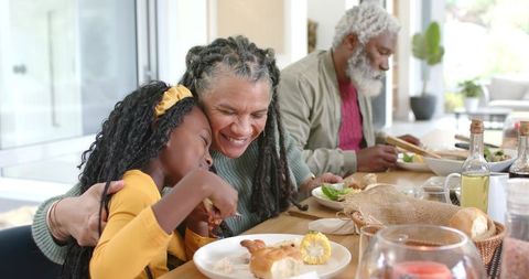 African American grandmother hugging granddaughter during multigenerational family dinner