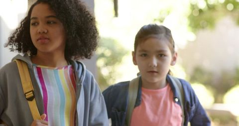 Young students carrying colorful backpacks walking into school under bright sunlight