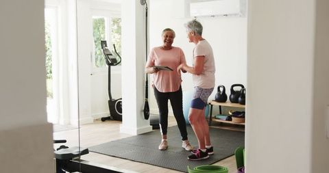 Senior multiracial lesbian couple using tablet at home gym