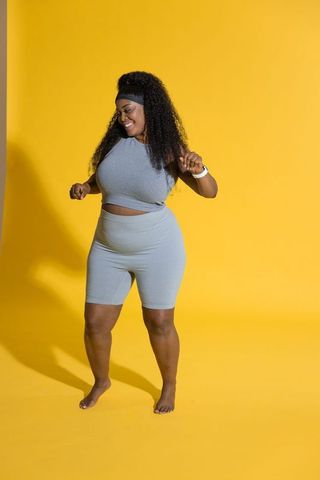 African american woman dancing in gray athleisure, showing smartwatch on yellow backdrop
