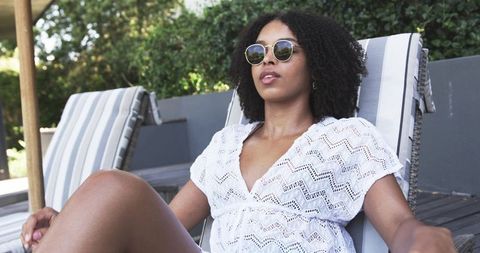 African woman relaxing on poolside lounge chair in white crochet dress and sunglasses