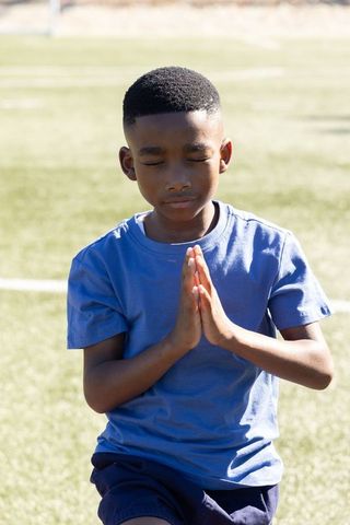 Young african american boy praying outdoors on sports field meditating in sunlight