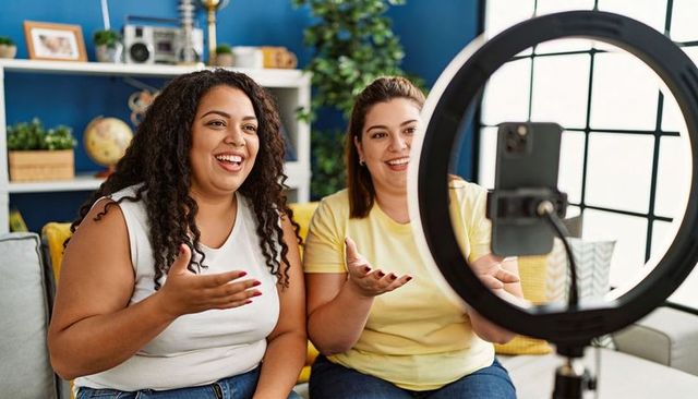 Two Women Livestreaming with Ring Light on Sofa Laughing and Hosting Casual Conversation